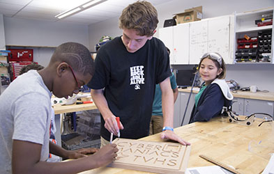 photo of three students carving letters in a block of wood.