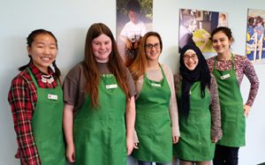 Photo of five students posing together in green aprons