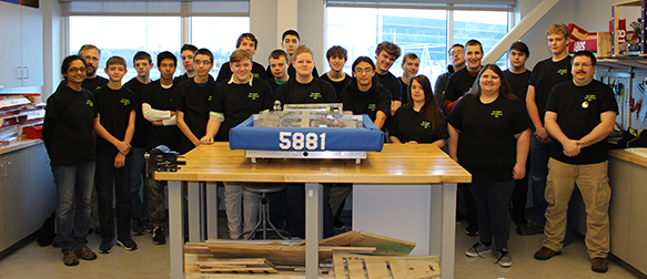 Photo of students around a table with a robot.