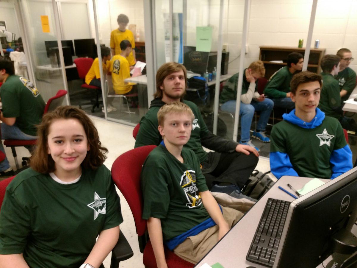 Group of students in green shirts sitting around a computer